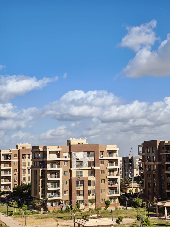 who-we-are Contemporary apartment complex with bright blue sky and clouds.